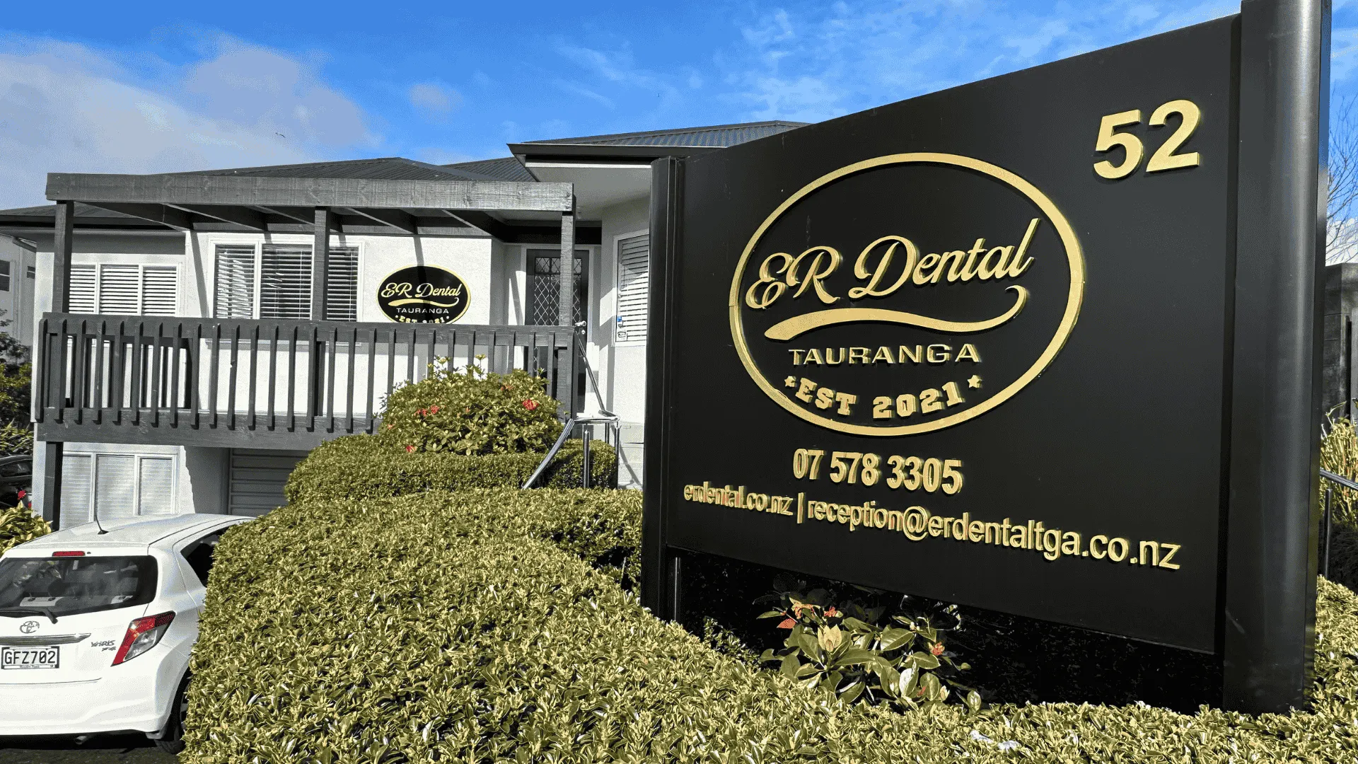 Dental clinic exterior with sign, plants, and parked car